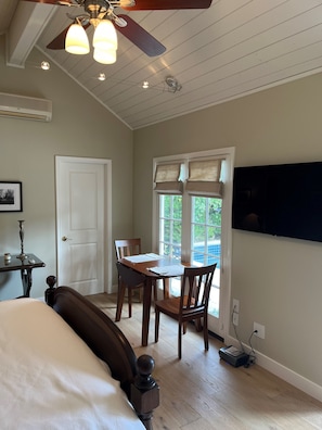Een slaapkamer met een bed, een bureau met stoel, een plafondventilator en een raam met jaloezieën.