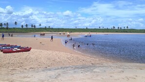 Une plage où l’on peut voir des kayaks alignés sur le sable, un bateau sur l’eau et des gens qui profitent de la plage.