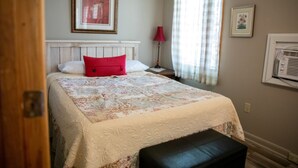 Un dormitorio con cama, mesita de noche, lámpara y ventana con cortinas.