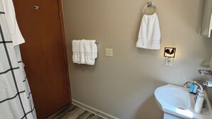 Une salle de bain avec un plancher en bois, un lavabo blanc et deux serviettes suspendues à des crochets.