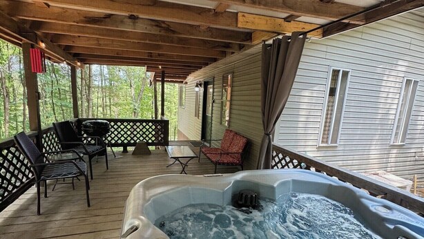 Terraza techada al aire libre con jacuzzi, mobiliario de madera y vista a una casa.