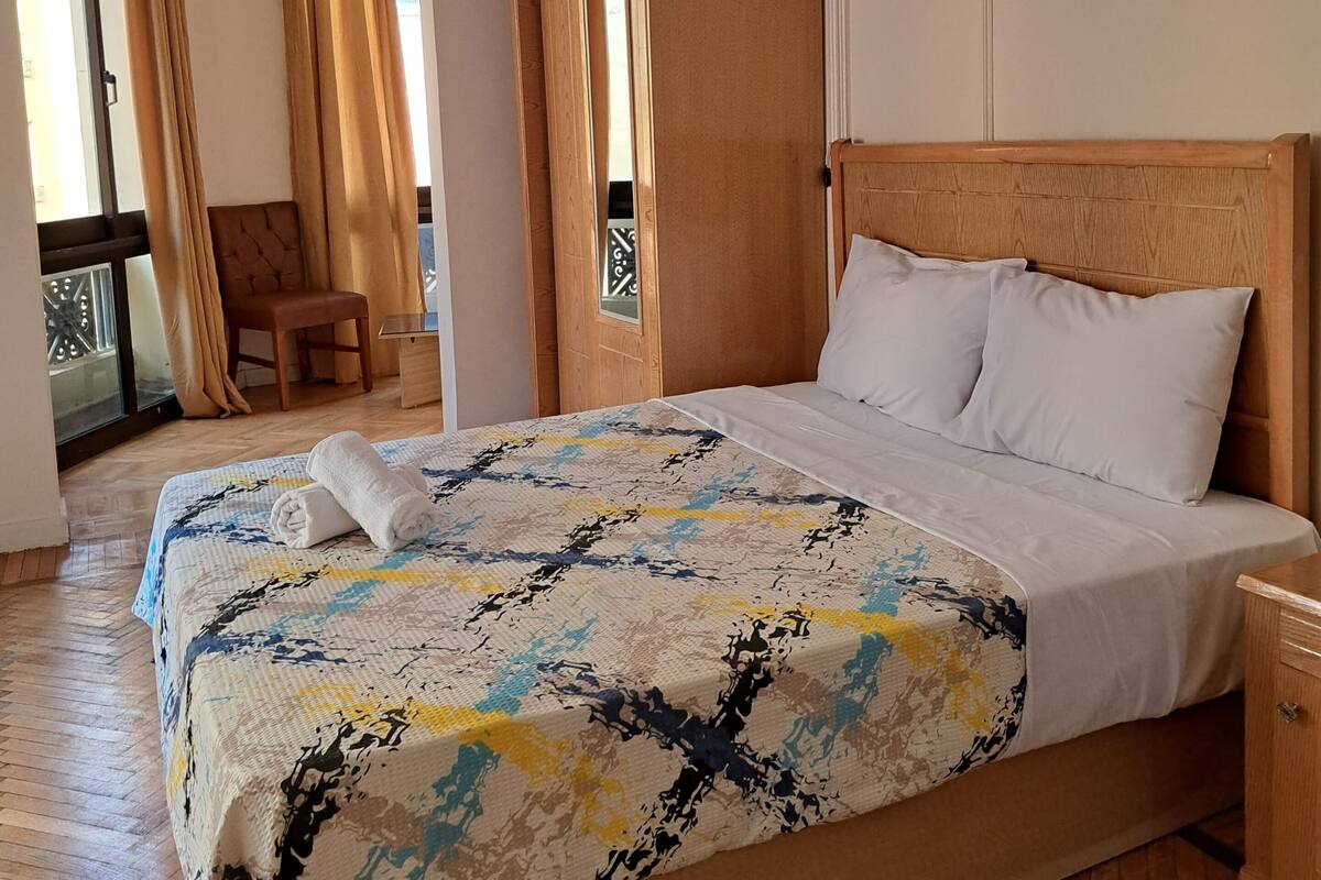 A neatly made bed with a patterned bedspread, a wooden headboard, and a nightstand.