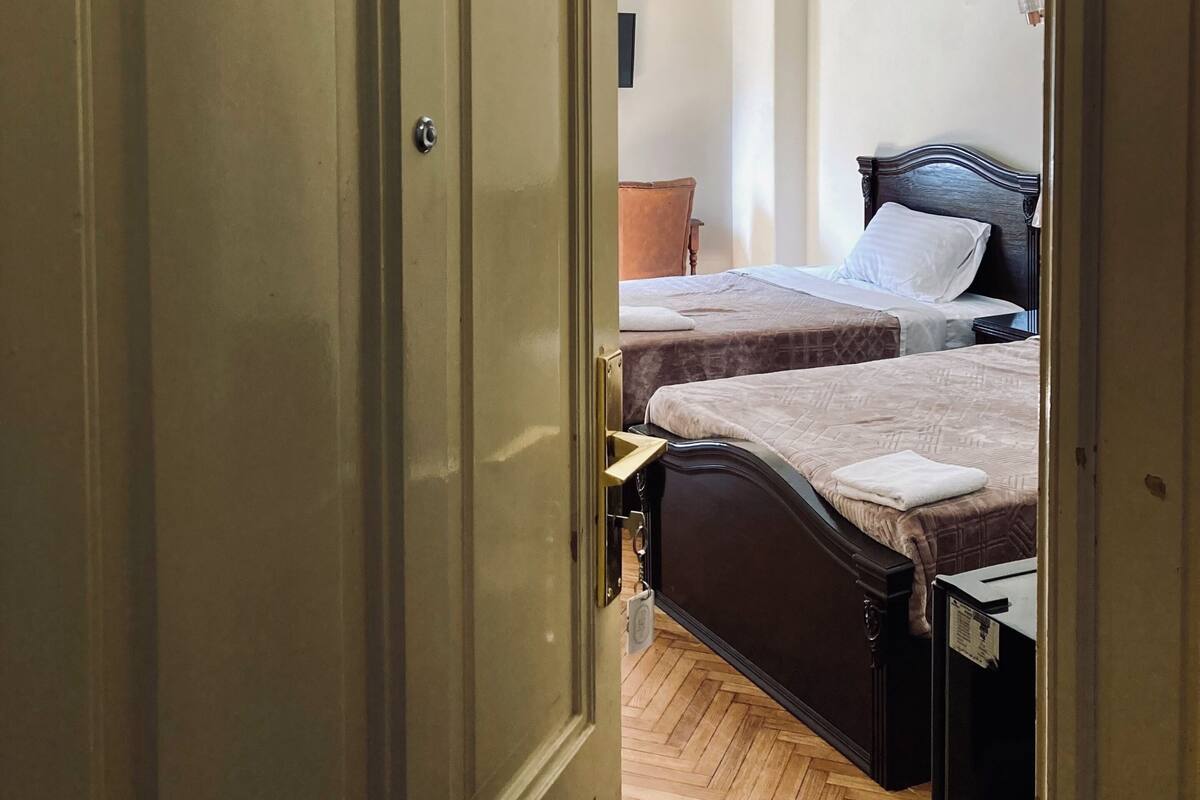 A hotel room with two beds, a wooden floor, a wardrobe, and a chandelier.