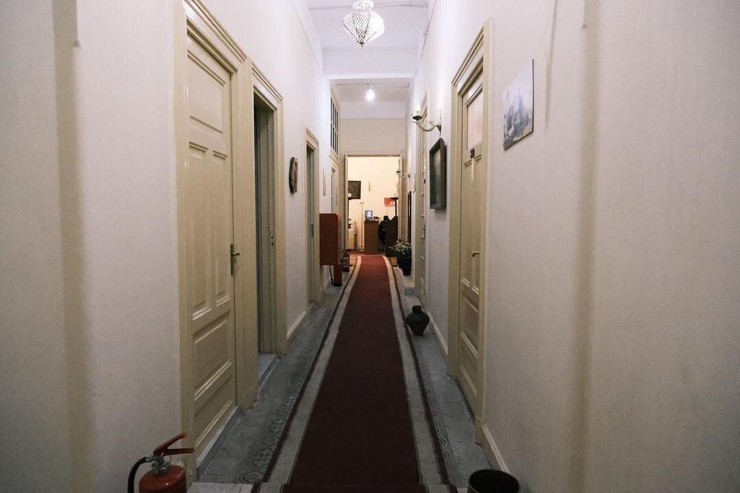 Un pasillo estrecho con puertas color beige, una alfombra roja y un extintor en la izquierda.