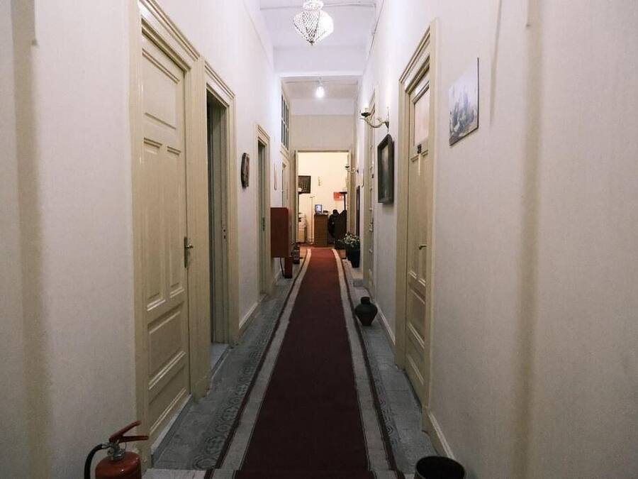Un pasillo estrecho con puertas color beige, una alfombra roja y un extintor en la izquierda.