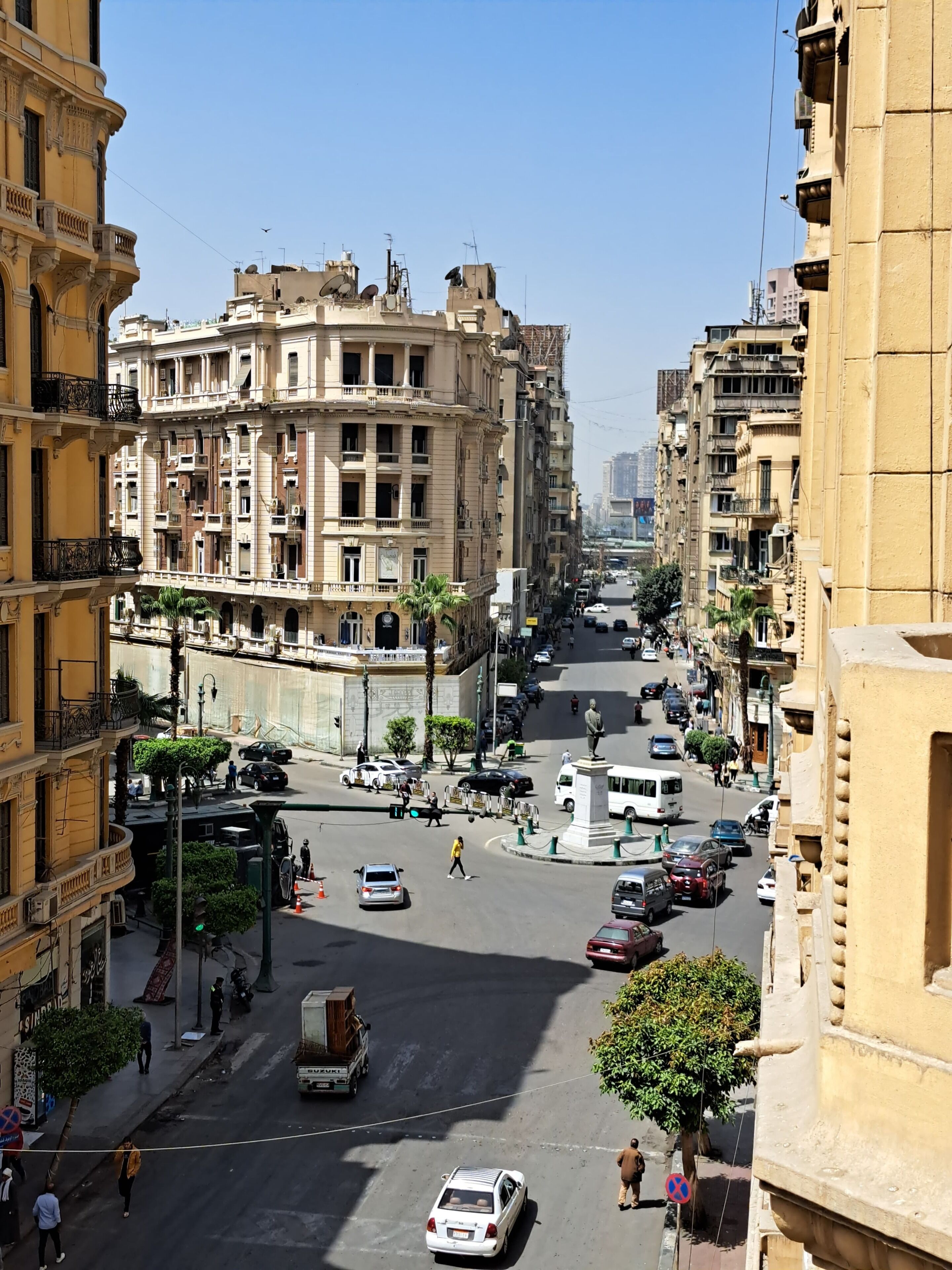 A street view of a city with multi-story buildings, a statue, and vehicles.