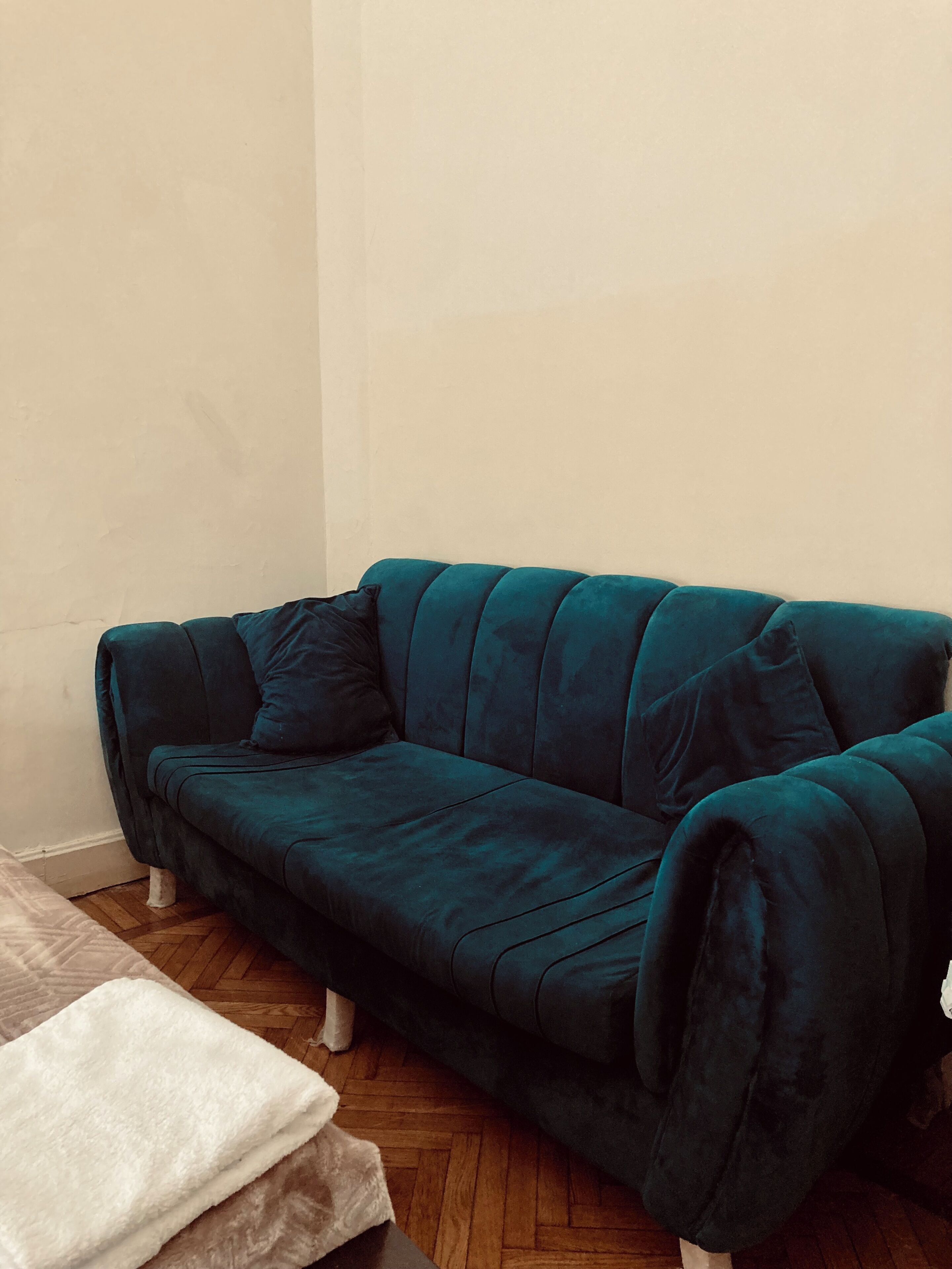 A teal sofa with a dark cushion, a white blanket, and a wooden floor.