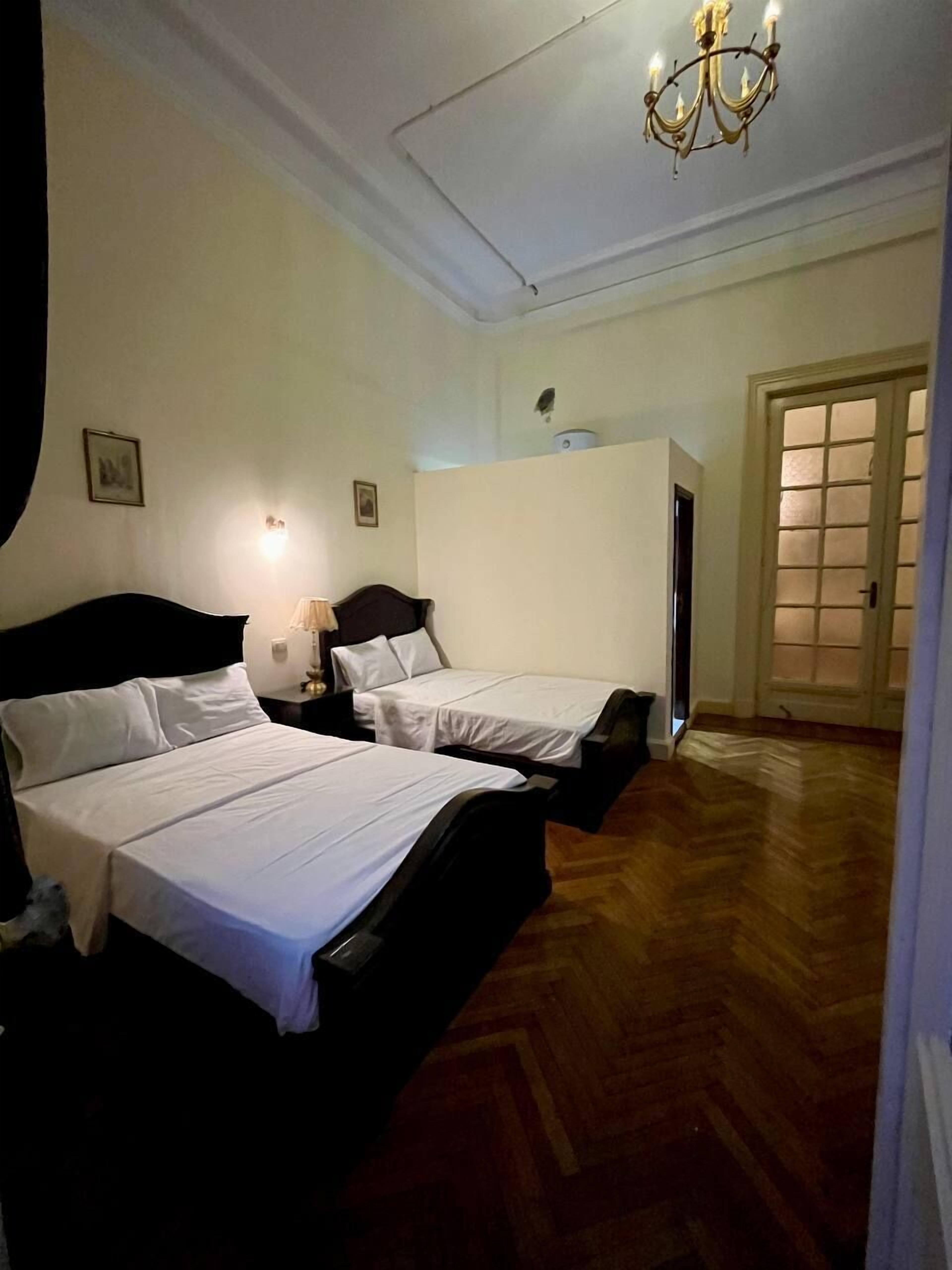 A hotel room with two beds, a chandelier, a wooden floor, and a door with glass panels.