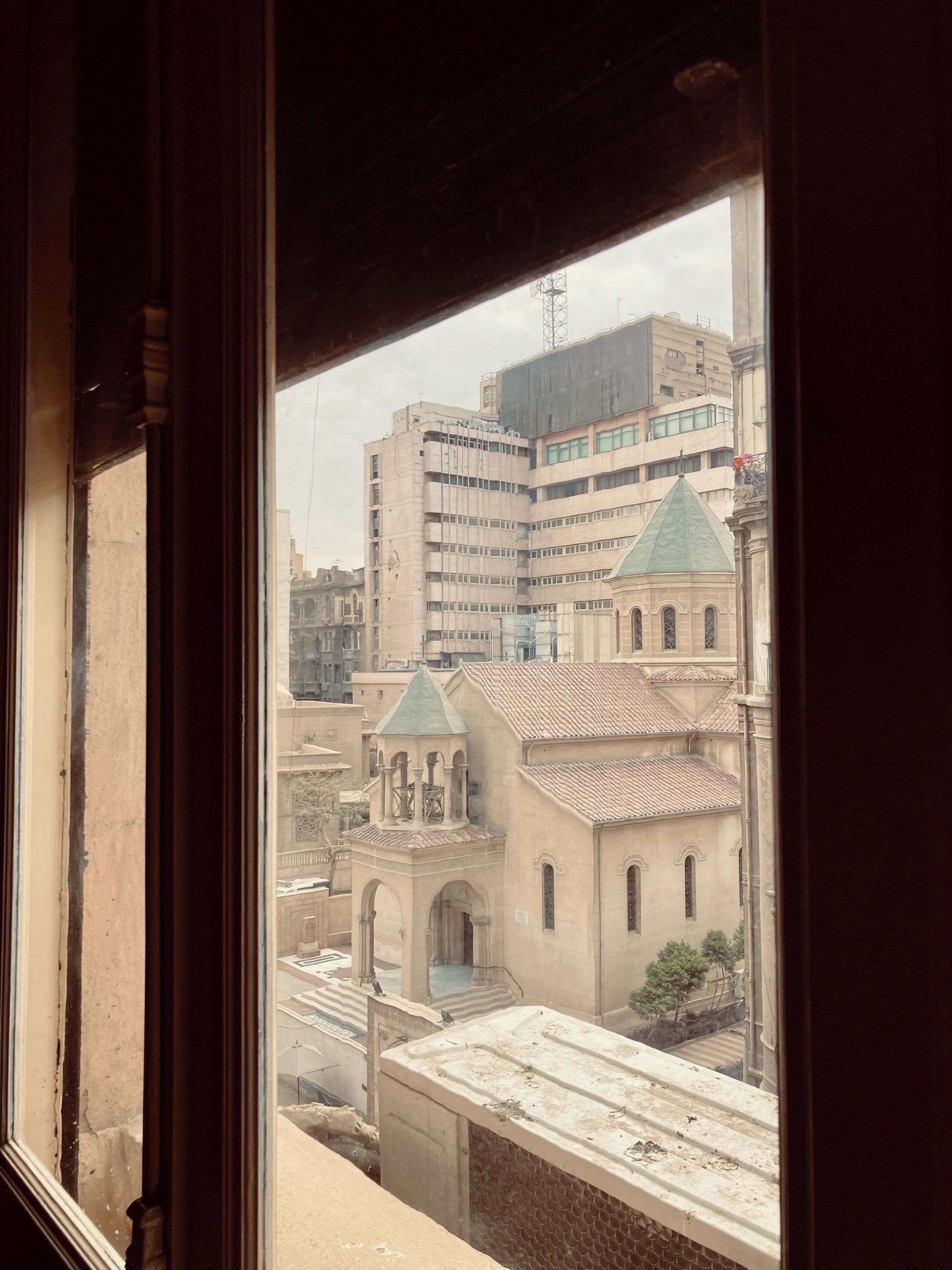 Une vue à travers la fenêtre d’un bâtiment doté d’un toit en tuiles et d’un clocher.