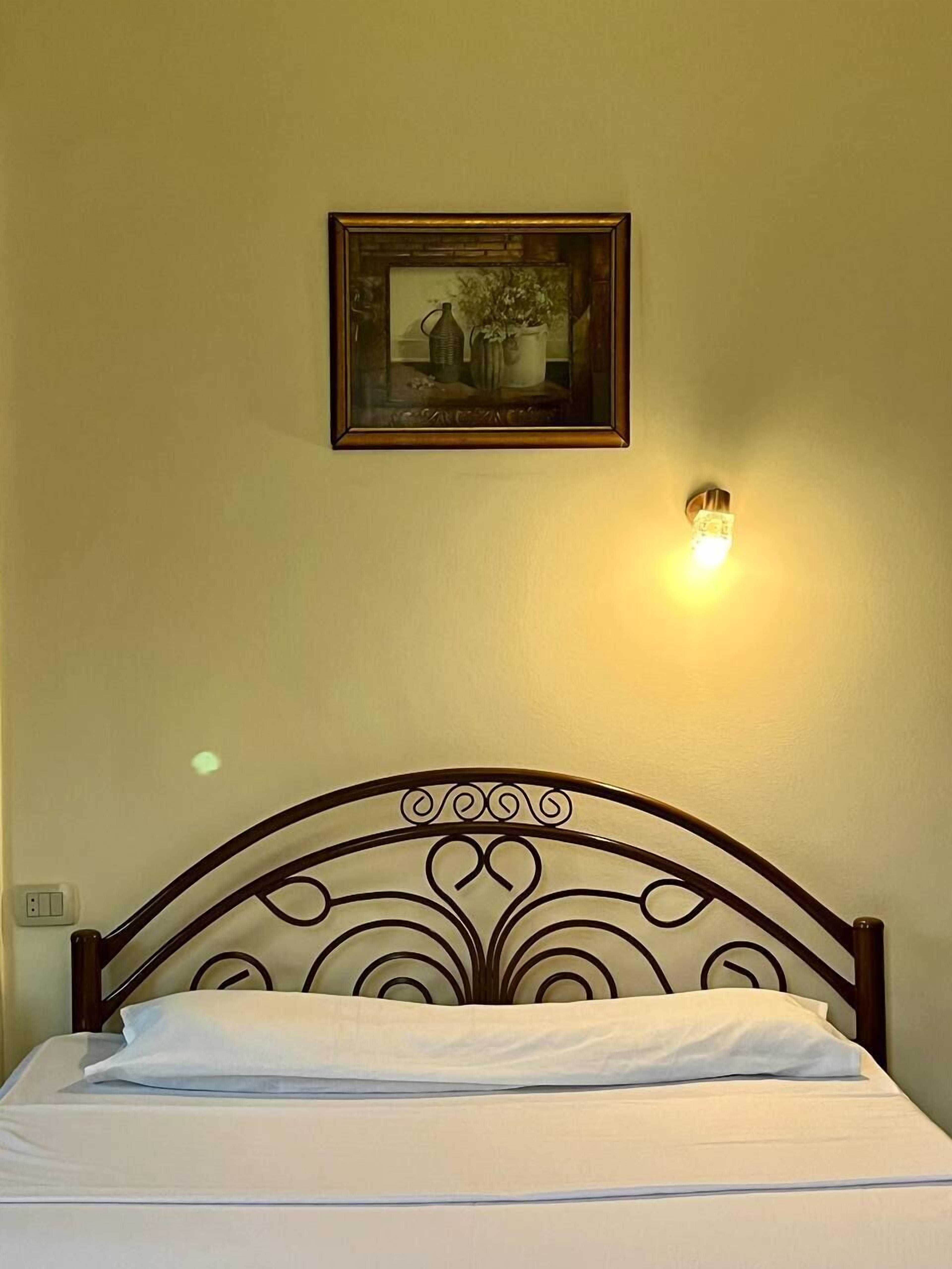 Ein Bett mit Metallkopfteil, ein gerahmtes Bild an der Wand und eine Wandleuchte.