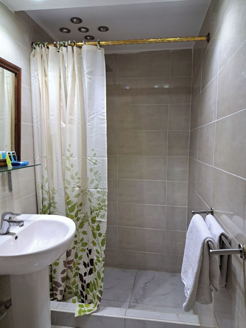 Un baño con ducha, lavamanos y un perchero para toallas.
