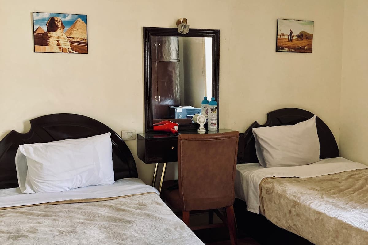 A hotel room with two beds, a desk with a mirror, and two wall-mounted paintings.