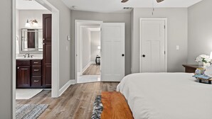 A bedroom with a large bed, a ceiling fan, and a view into the bathroom with a mirror and sink.