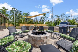 An outdoor patio with a stone fire pit, wicker furniture, and a grill.