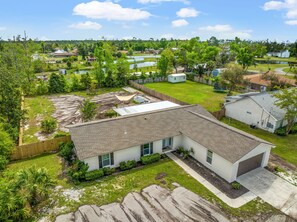 A residential area with a single-story house featuring a garage, a fenced yard, and a pond.