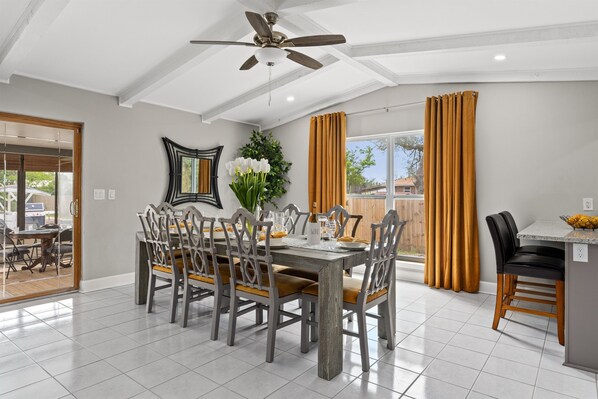 A dining area with a wooden table and chairs, a ceiling fan, and a view of the outside.