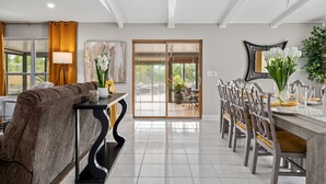 A modern dining area with a long table, chairs, and a view through glass doors to an outdoor patio.
