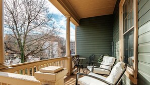 A covered porch with a wooden railing, a stone bench, and two chairs with cushions. - The Serendipity Suite: Desk, EV, Walk Downtown (Staunton)