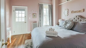 A bedroom with a bed, a radiator, a door, and a window with curtains. - The Serendipity Suite: Desk, EV, Walk Downtown (Staunton)