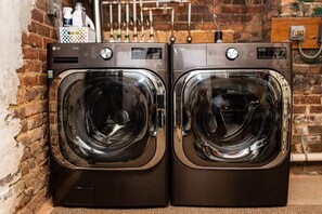 Two LG Thinx front-loading washing machines in a laundry area with a brick wall and a metal rack in the background.