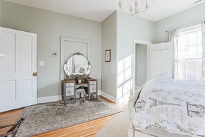 Quarto com cama, cômoda, espelho e janela.