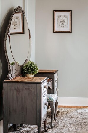 A vintage dresser with a mirror, a small plant, and a framed picture on the wall.