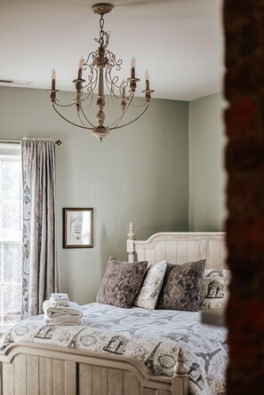 A bedroom with a bed, a chandelier, a window with curtains, and a framed picture on the wall.