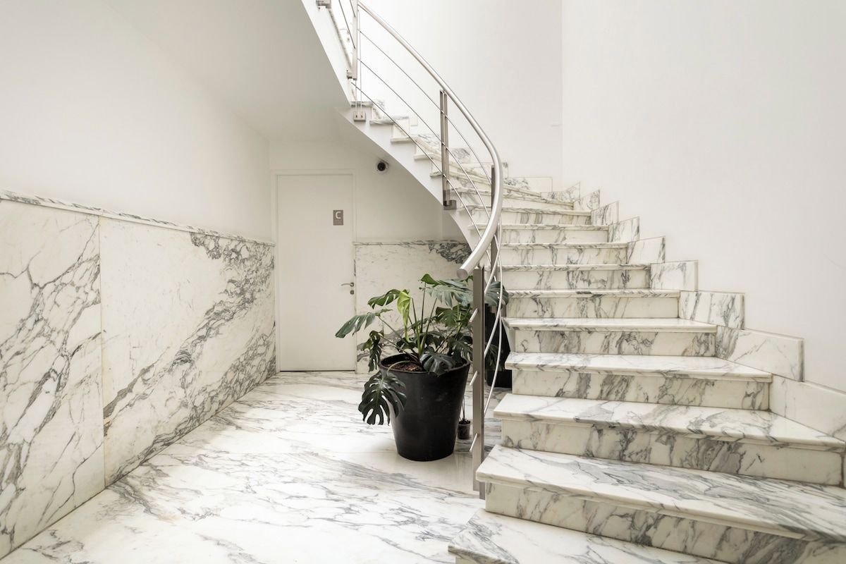 Un escalier en marbre avec une rampe métallique menant à une porte marquée d’un « C ».