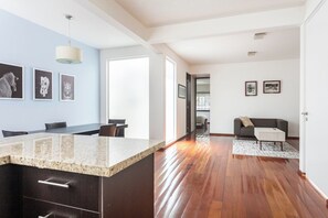 A modern kitchen with a granite countertop and dark cabinetry, leading to a living area with a sofa and a coffee table.