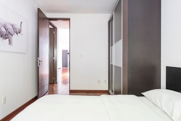 A bedroom with a bed, a door leading to another room, and a wall-mounted artwork.