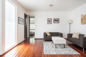 A modern living room with hardwood flooring, a gray sofa, a white coffee table, and a patterned rug.