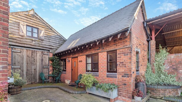 Een bakstenen huis met een houten deur, een klein portaal en een tuin met planten in potten.