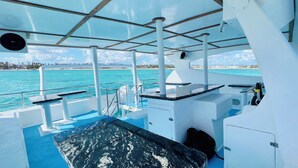 Un pont de bateau offrant une vue dégagée sur des eaux turquoise et une plage au loin.