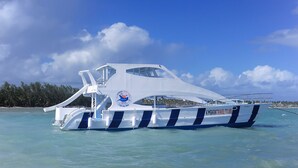 Un bateau blanc à rayures bleues, portant l’inscription « KIMBARAT TRAVEL TOURS » sur sa coque, flotte sur une eau turquoise et cristalline.