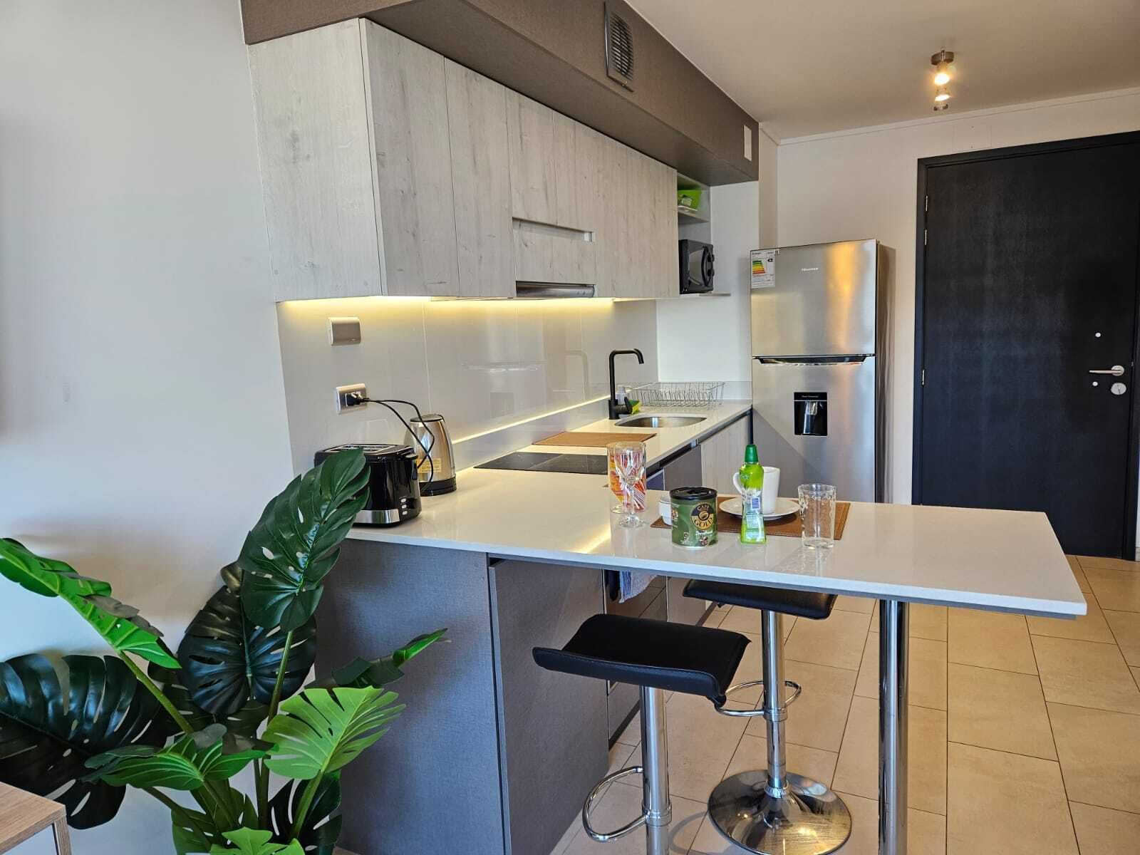 Une cuisine moderne avec un plan de travail blanc, des appareils en acier inoxydable et un tabouret de bar.