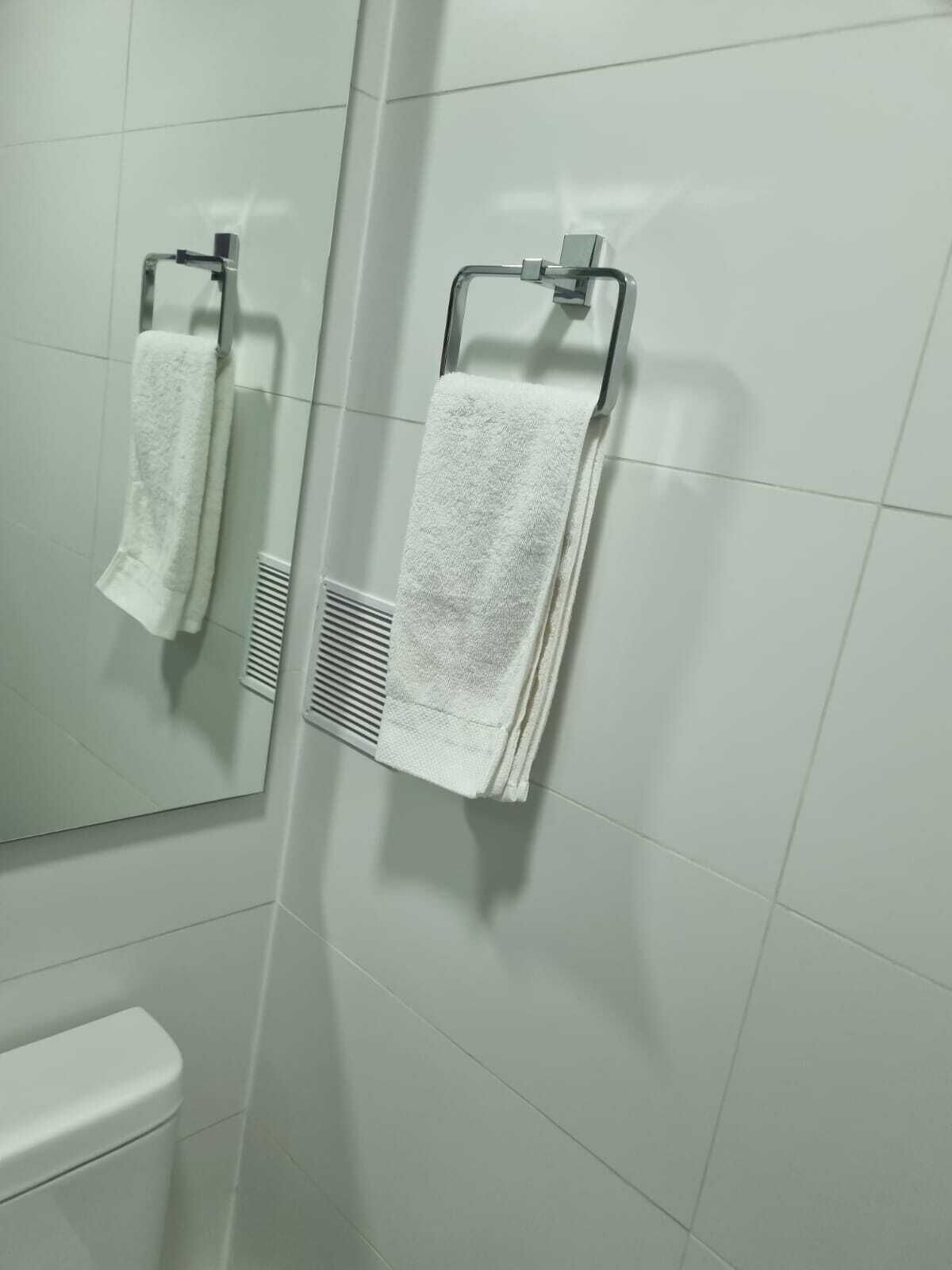 Un baño con paredes de azulejos blancos, un inodoro y dos toallas colgadas en toalleros.