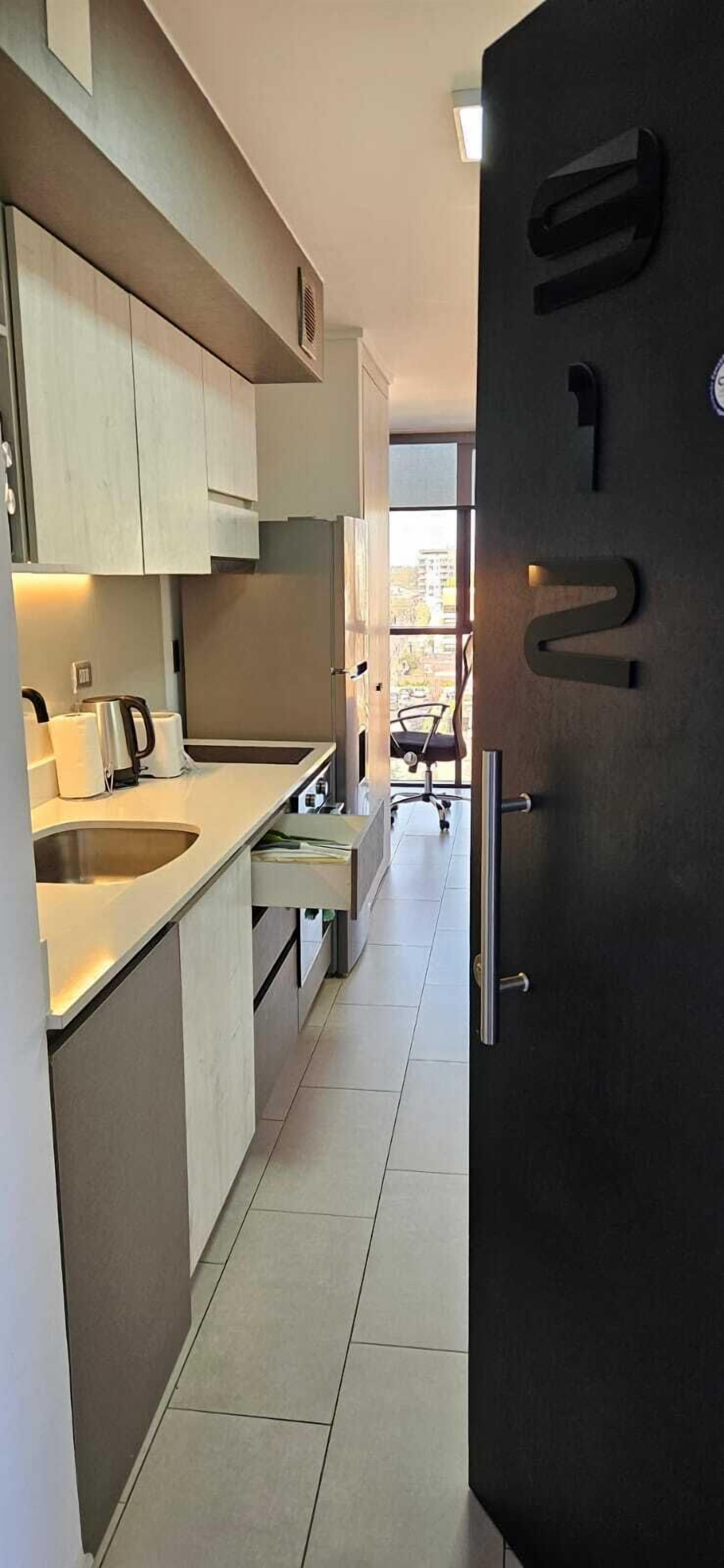 A modern kitchen with light wood cabinets, a stainless steel sink, and a black refrigerator.