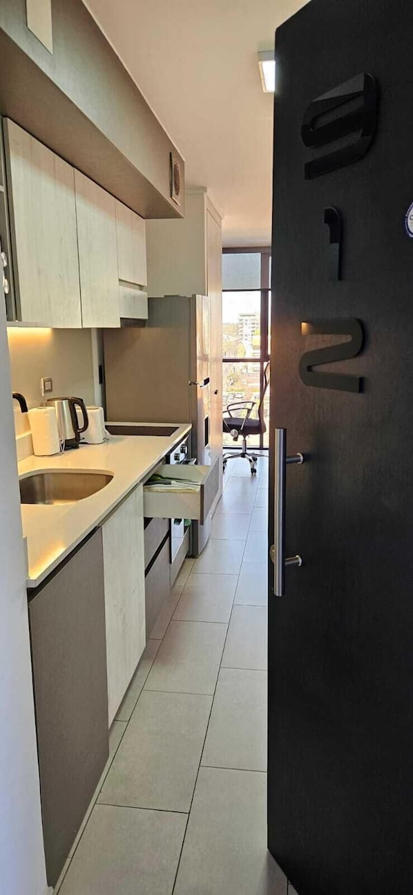 Una cocina moderna con armarios de madera clara, un lavamanos de acero inoxidable y un refrigerador negro.