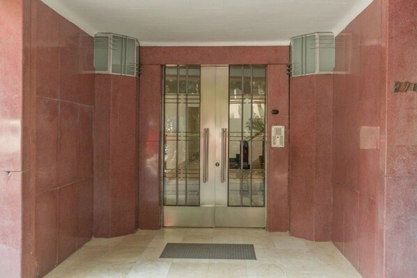 A building entrance with a glass door, a metal gate, and a number plaque.