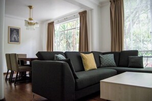 A modern living room with a dark-colored sofa, a wooden coffee table, and a dining area with chairs.