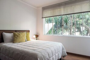 A bedroom with a bed, a nightstand, a lamp, and a window with blinds.