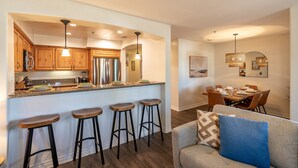 A modern kitchen with wooden cabinets, a stainless steel refrigerator, and a bar area with stools. - Newly Designed 2-Story Condo - 1 Block to the Beach! (San Diego)
