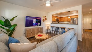 A modern living room with a grey sofa, a coffee table, and a TV mounted on the wall. - Newly Designed 2-Story Condo - 1 Block to the Beach! (San Diego)