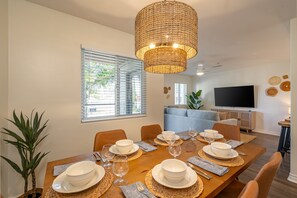 Een eetgedeelte met een houten tafel voor vier personen, omringd door stoelen, met een geweven hanglamp erboven.