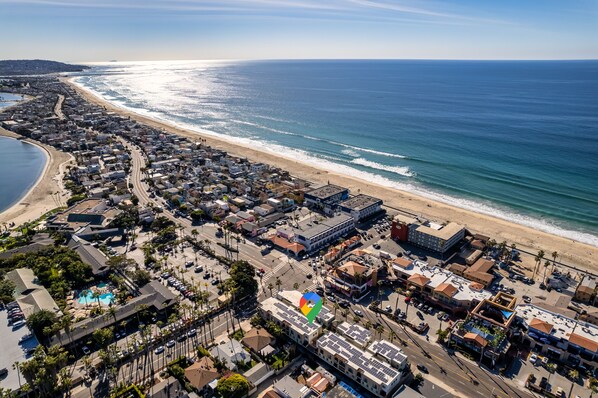 Luchtbeeld van een kustplaatsje met een strand, woonwijken en een hotel met zwembad.
