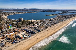 Vue aérienne d’une ville côtière avec une plage, des bâtiments et un port de plaisance.