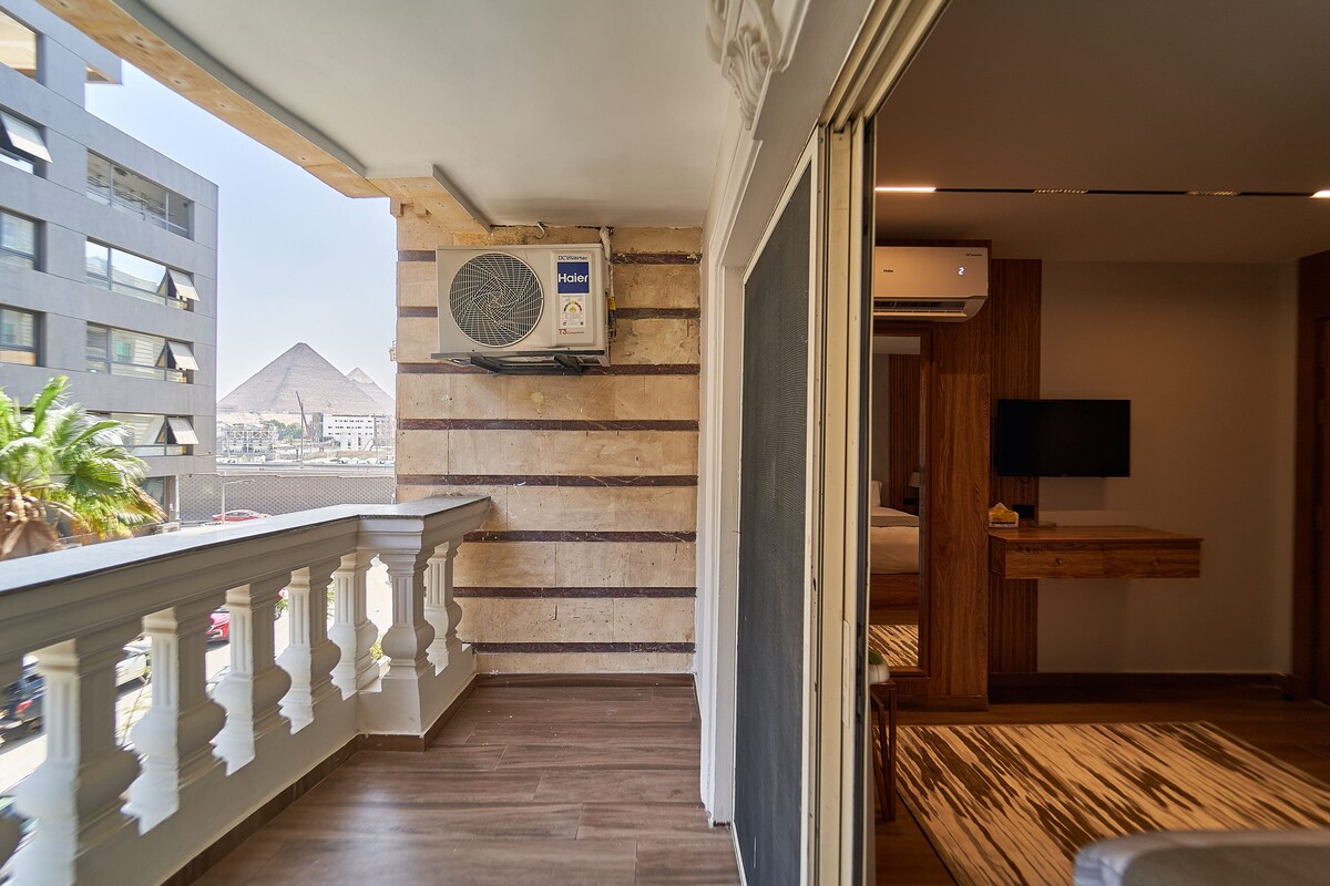 A balcony with a view of a pyramid, an air conditioning unit, and a wooden floor.
