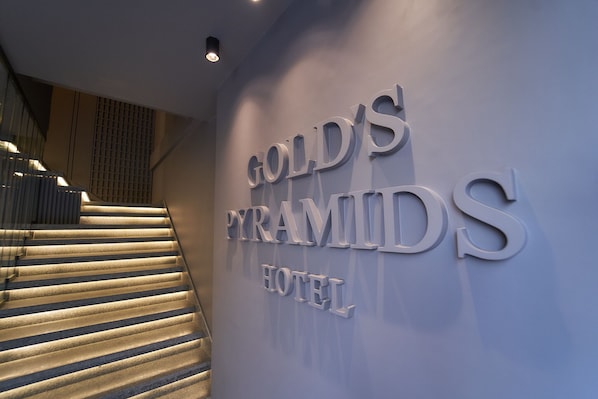 Una escalera conduce a la entrada de un hotel, donde se lee el nombre 'Gold's Pyramid Hotel'.