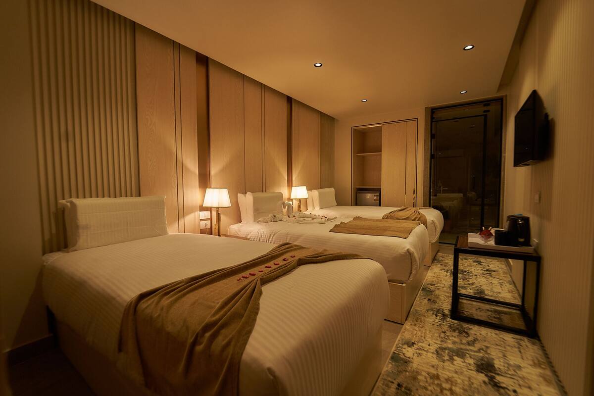 A hotel room with two beds, a small table with a coffee maker, and a TV mounted on the wall.