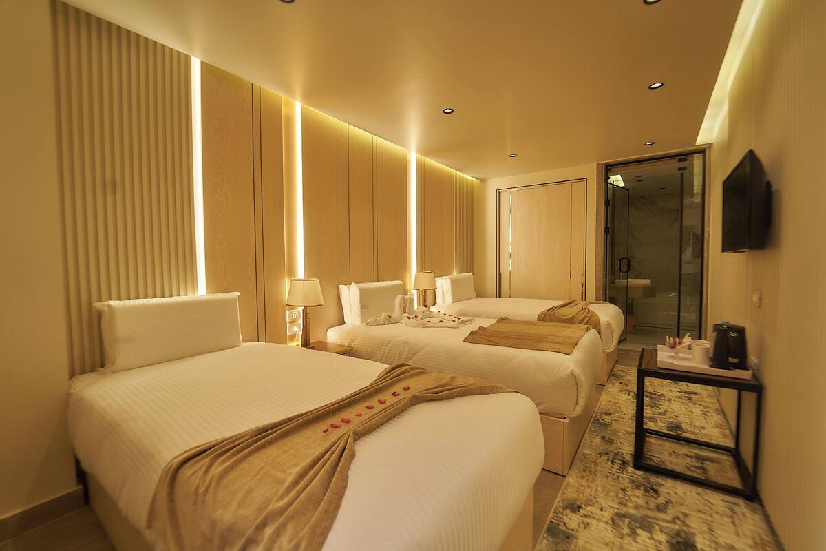 A hotel room with two beds, a bedside table with a lamp, a mirror, and a door leading to a bathroom.